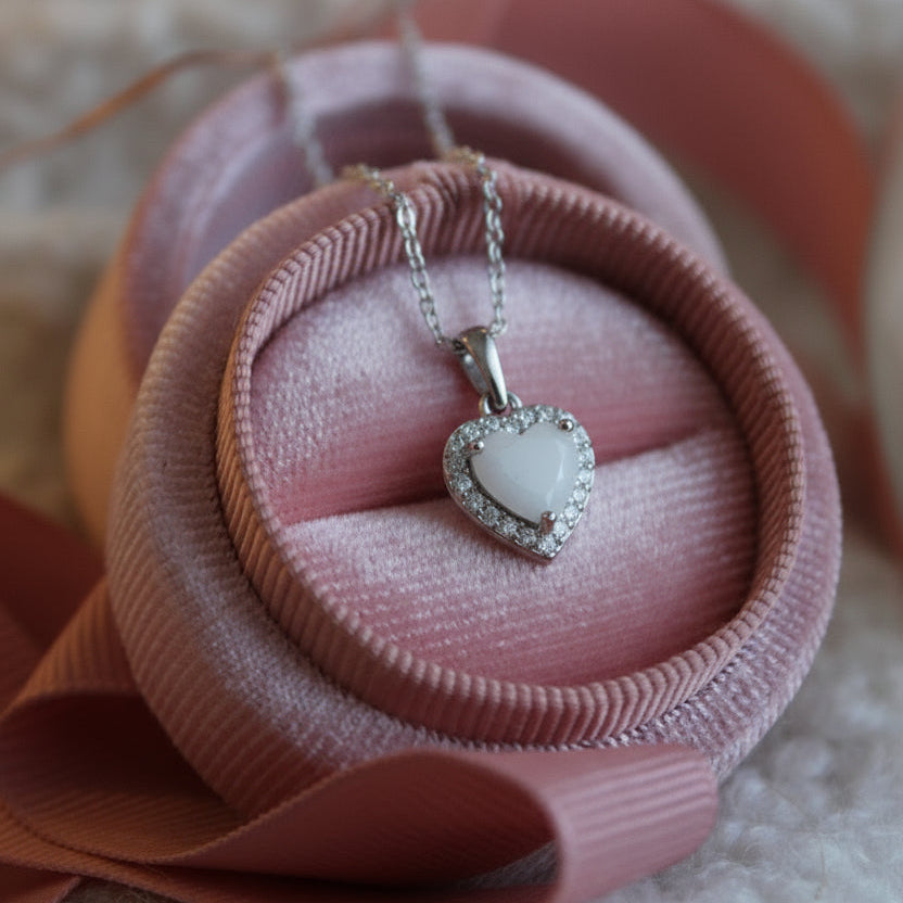 Heart-shaped pendant necklace on a pink ribbon with blurred lights in the background

